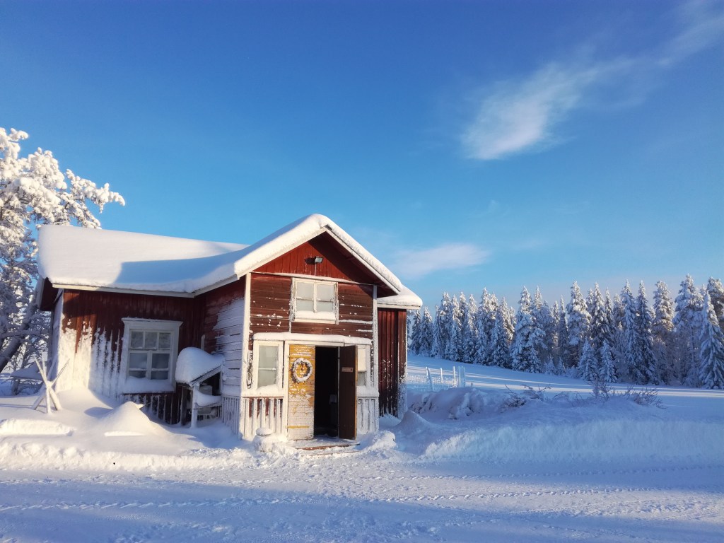 Vanha punainen talo pakkaspäivänä, luminen kuusimetsä taustalla.